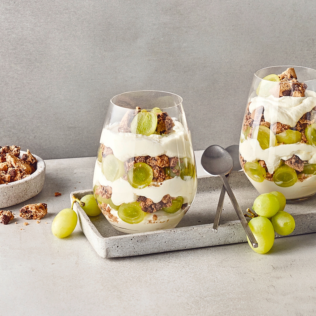 Dessertgläser, gefüllt mit Schichten aus heller Creme, grünen Weintrauben und gebröselten Keksen mit Schokostückchen