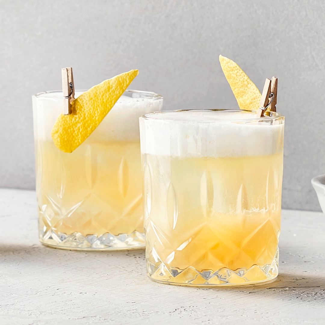 Zwei zitronige Cocktails mit einem schaumigen Topping und Zitronenscheiben.