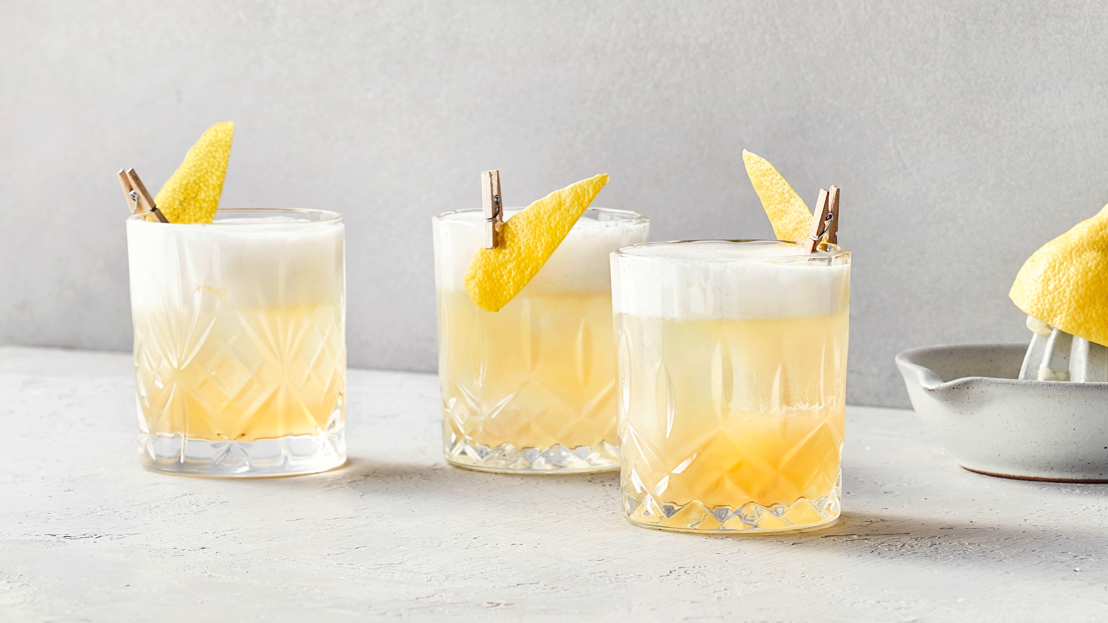 Drei zitronige Cocktails mit einem schaumigen Topping und Zitronenscheiben.