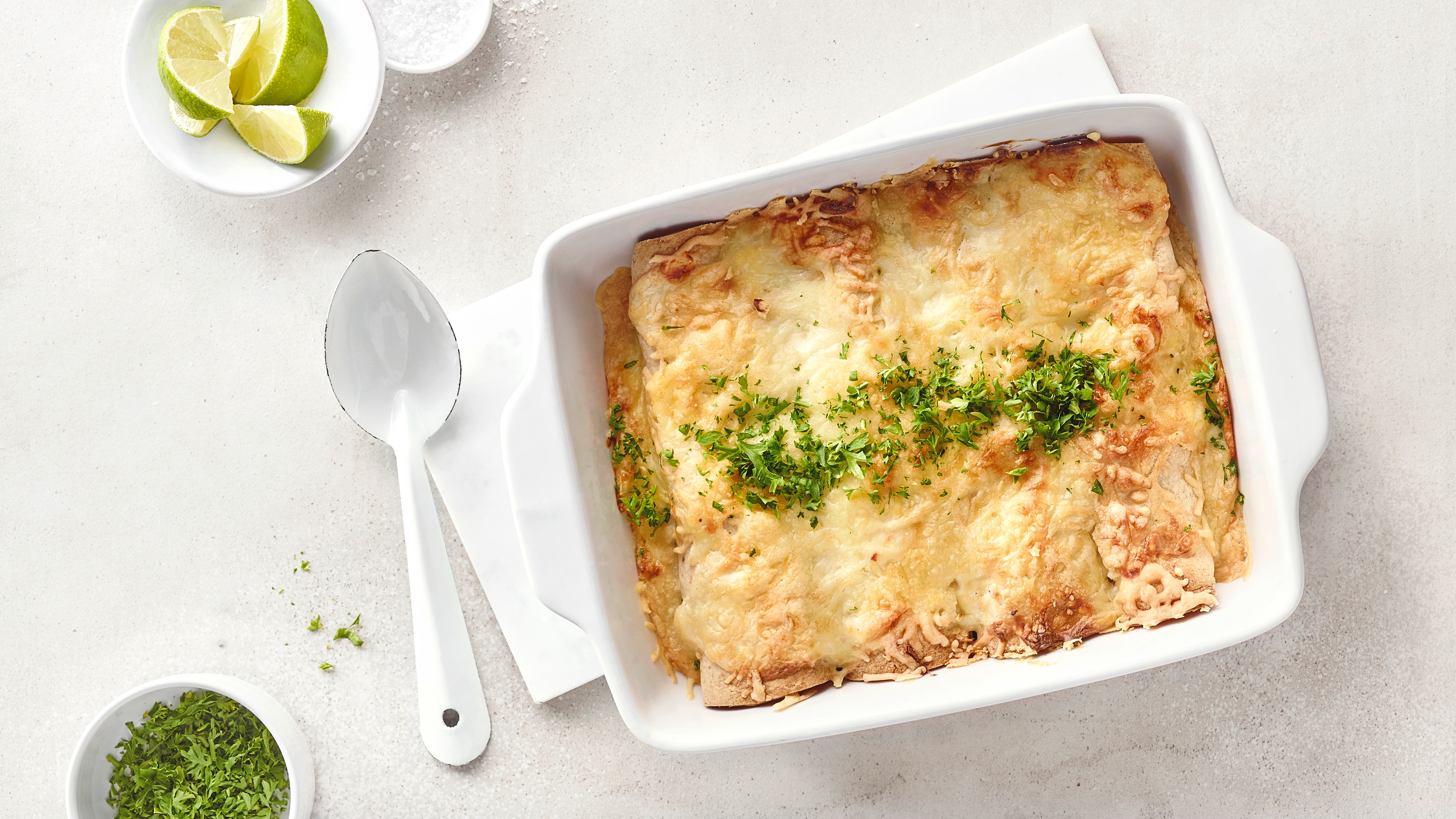 Überbackene Enchiladas mit geschmolzenem Käse und Kräutern in einer weißen Auflaufform.