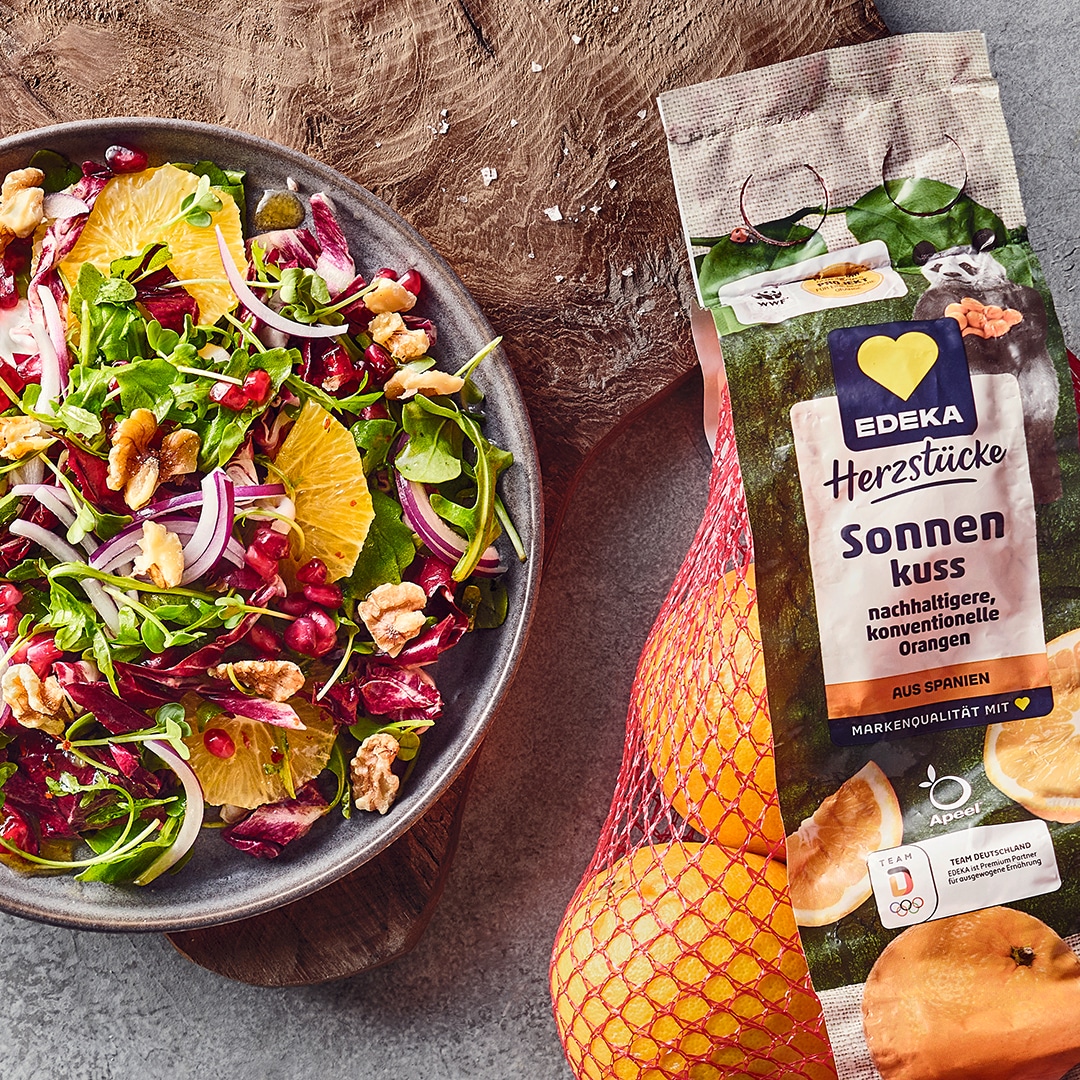 Ein Teller mit buntem Salat aus grünen Blättern, roten Zwiebelstreifen, Orangenscheiben, Walnüssen und roten Kernen