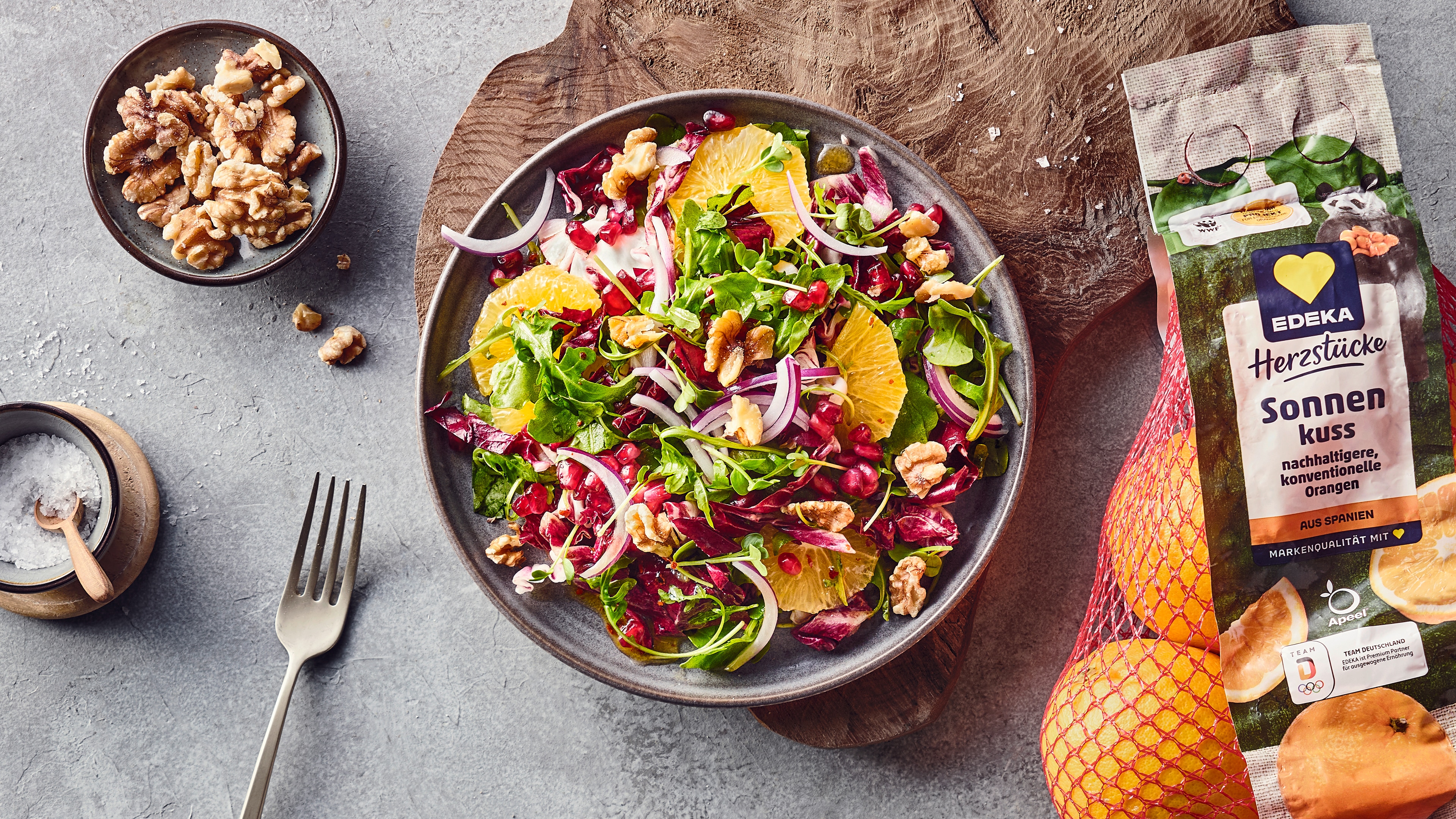 Ein Teller mit buntem Salat aus grünen Blättern, roten Zwiebelstreifen, Orangenscheiben, Walnüssen und roten Kernen