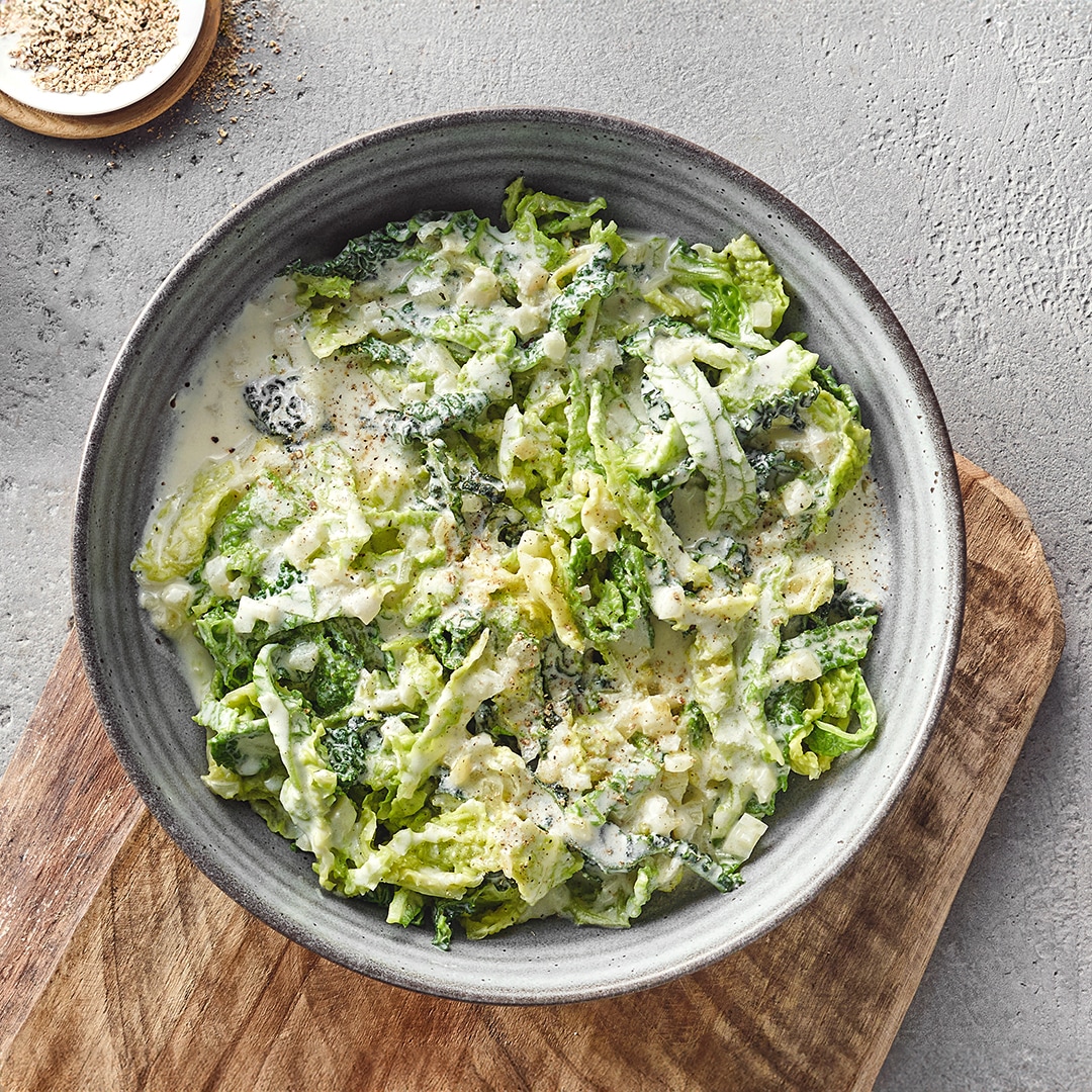 Ein Teller mit grünen Wirsingstreifen in weißer cremiger Soße, bestreut mit etwas schwarzem Pfeffer.