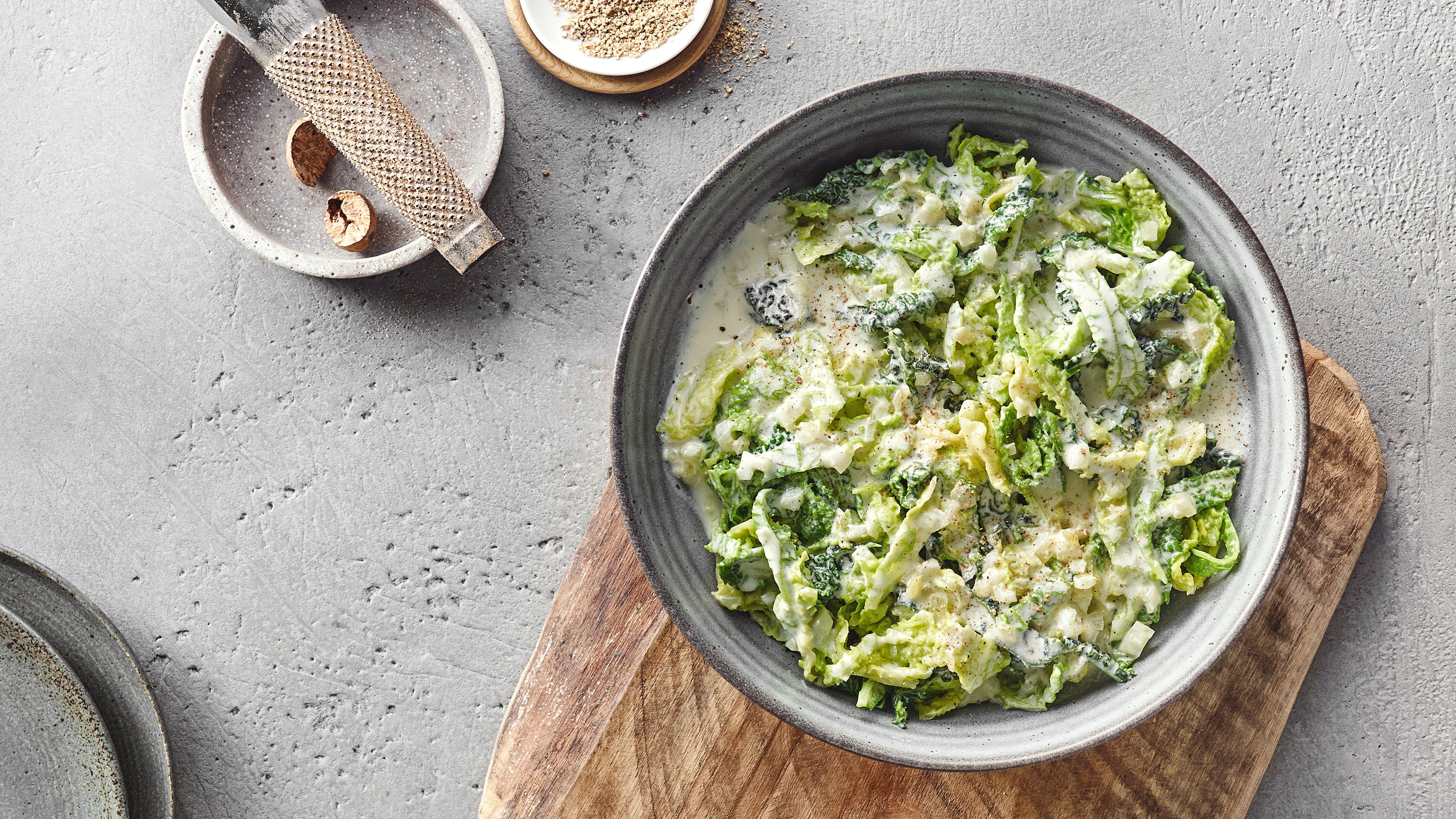 Ein Teller mit grünen Wirsingstreifen in weißer cremiger Soße, bestreut mit etwas schwarzem Pfeffer.