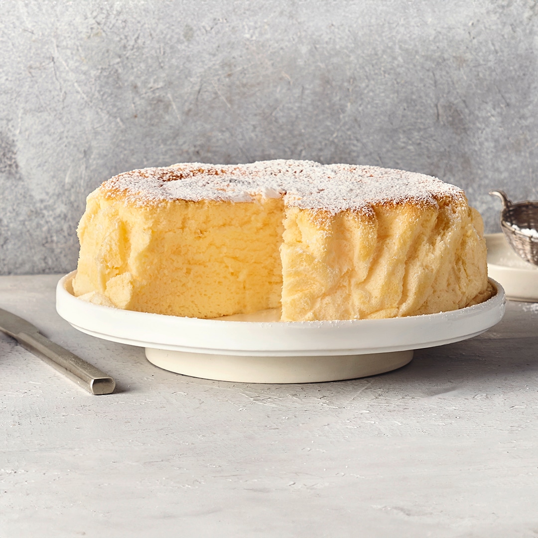 Ein Teller mit einem luftigen, hellgelben Kuchen, bedeckt mit einer Schicht weißem Puderzucker