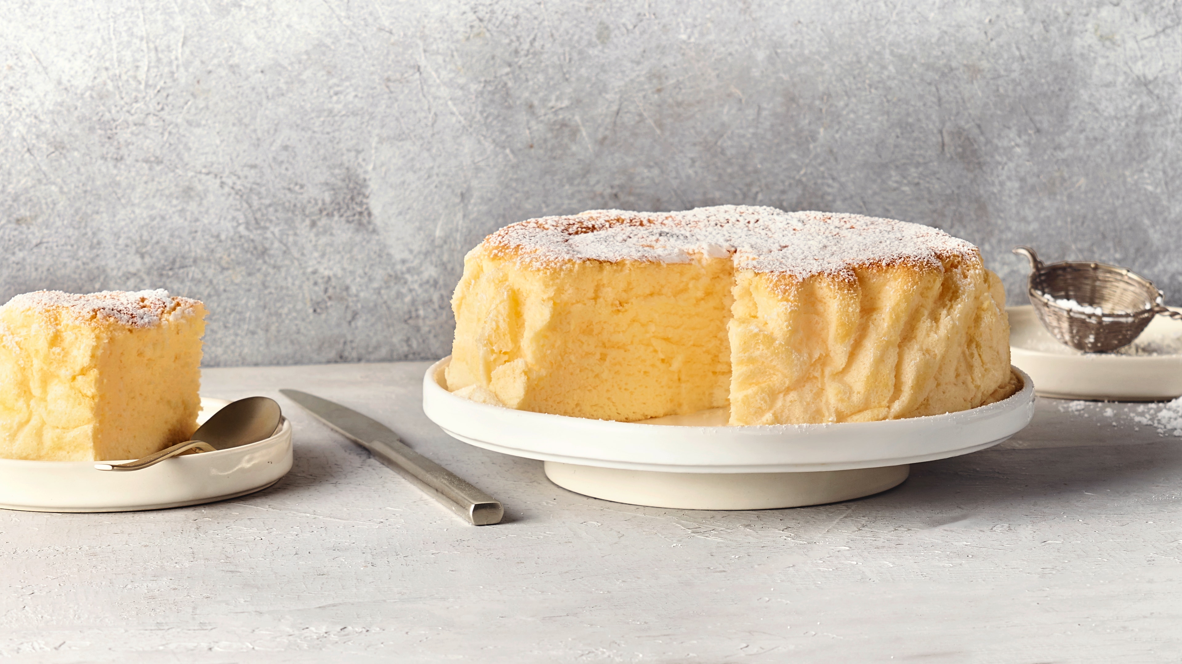 Ein Teller mit einem luftigen, hellgelben Kuchen, bedeckt mit einer Schicht weißem Puderzucker