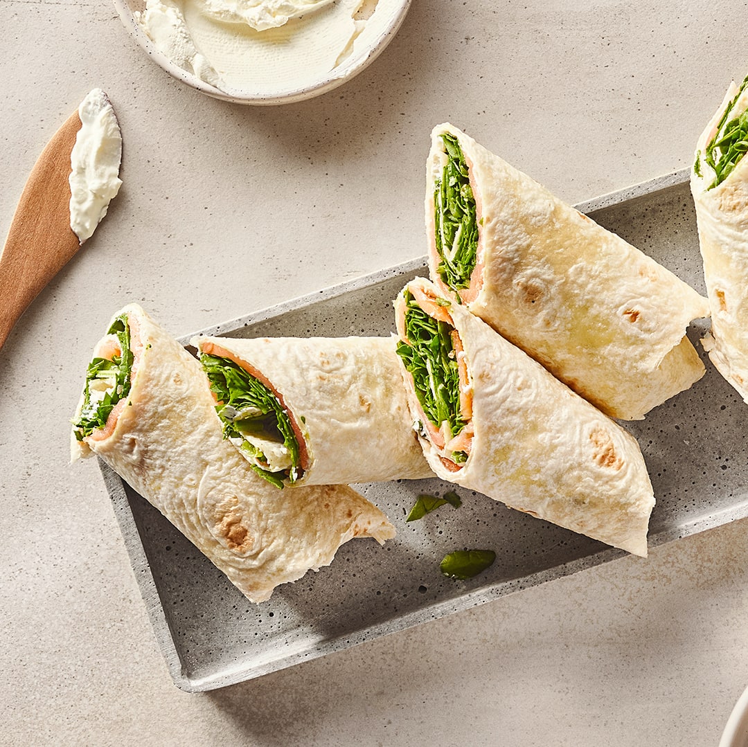 Wrap-Hälften gefüllt mit Salat, Lachs und Frischkäse, auf einem länglichen Tablett.