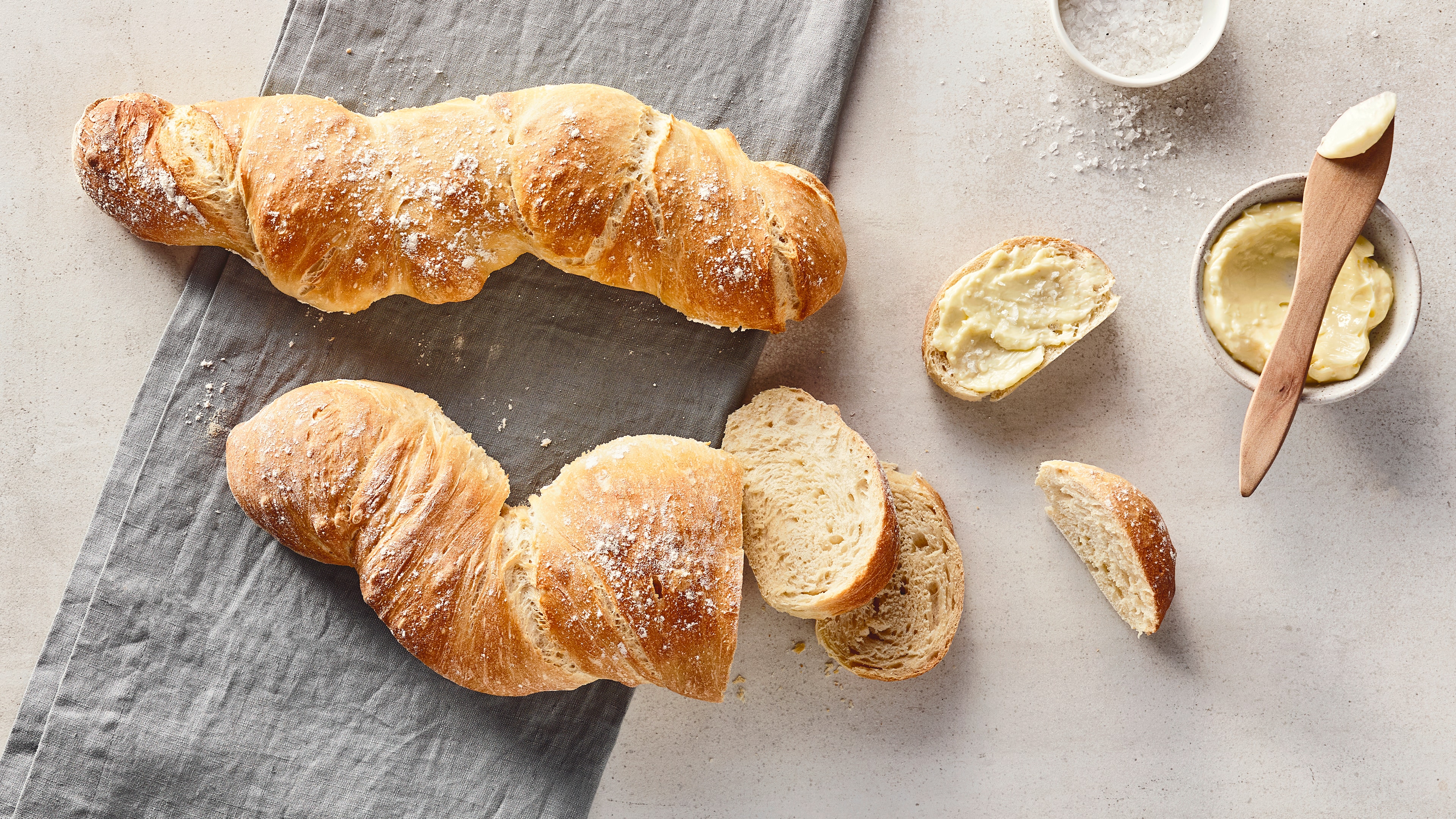 Gelbgold gebackenes, längliches, verwurzeltes Brot mit einer hellen und fluffigen Krume, auf einer hellen Steinplatte