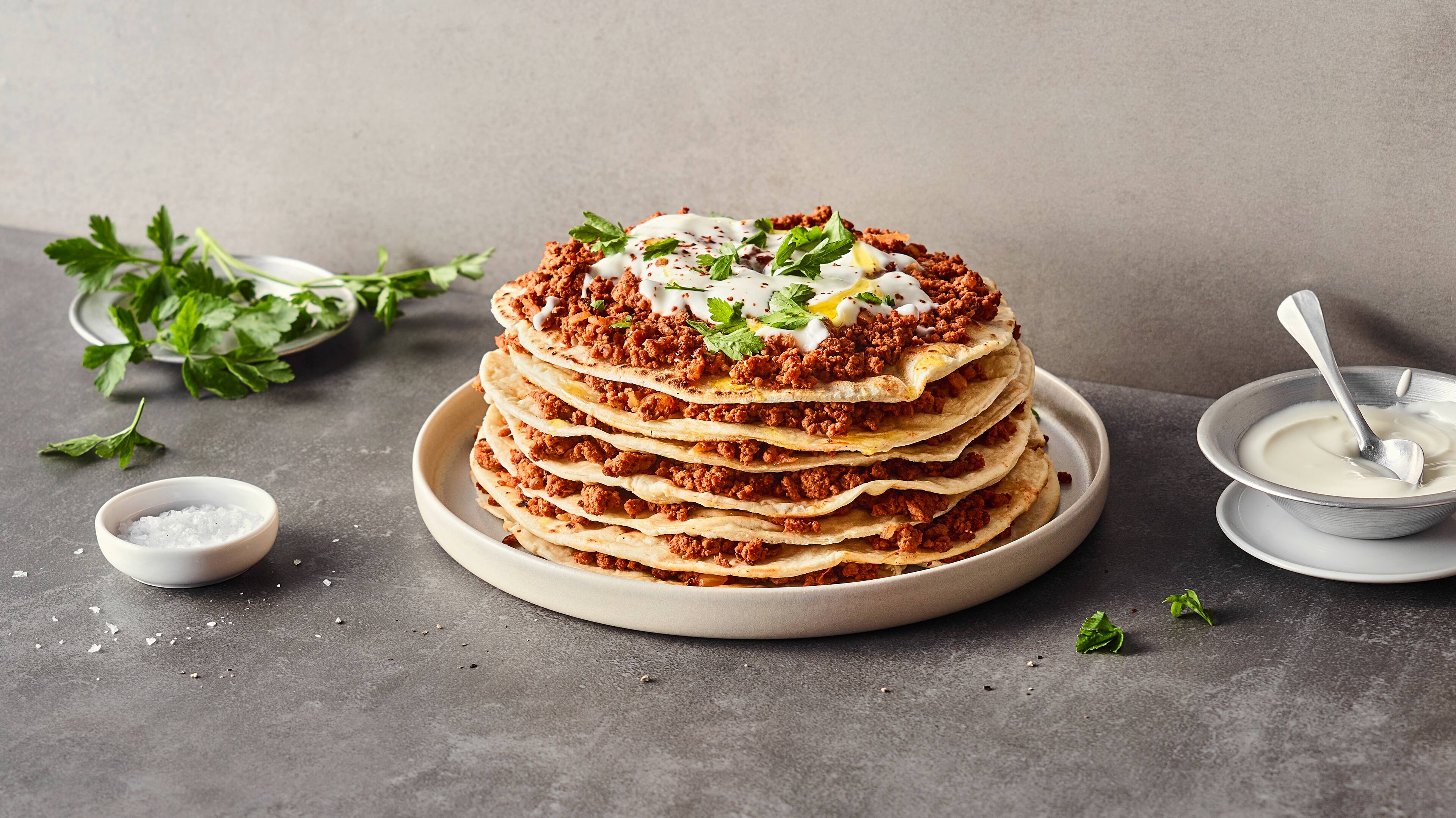Rezept für türkisches Yaglama Auf einem Teller ein Lasagne-Turm aus geschichten dünnen Fladenbroten und Hackfleisch, getoppt mit leichter Joghurtsoße