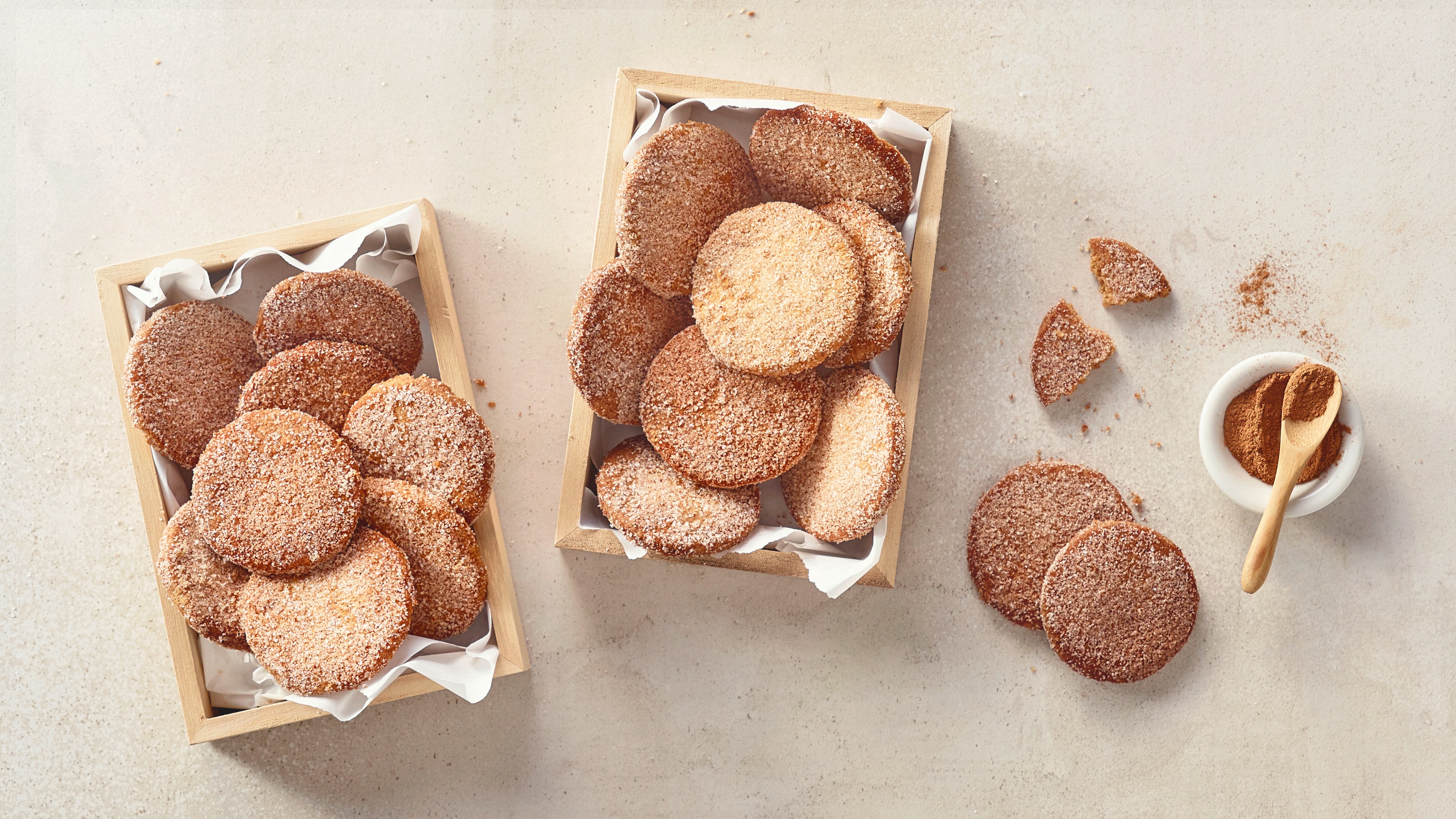 Eine Holzschale mit runden Keksen, mit Zucker bestreut, daneben zerbrochene Stücke und eine kleine Schale mit Zimt