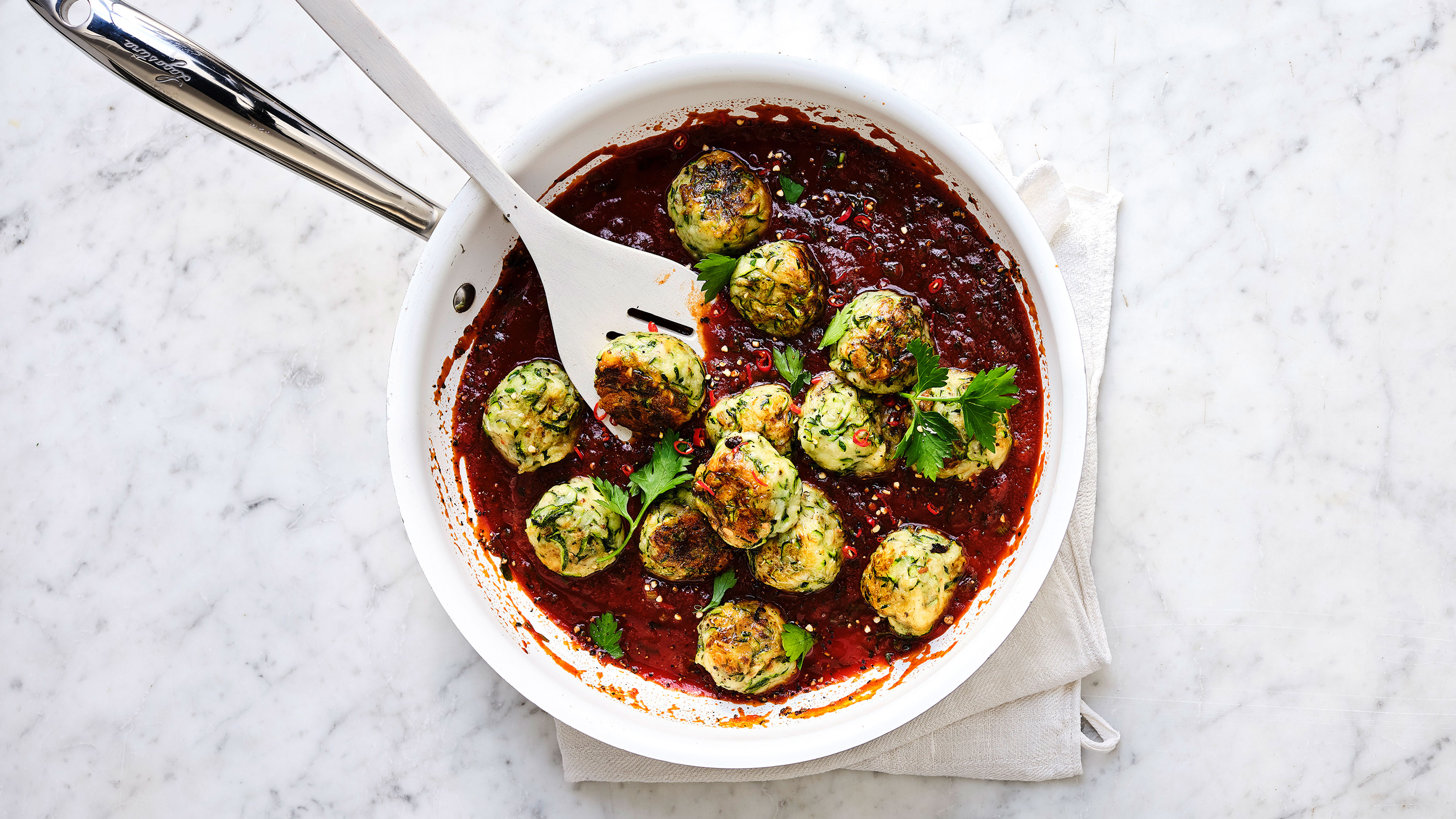 Kleine goldbraun gebratene Gemüsebällchen in Tomatensauce mit Kräutern in einer weißen Pfanne.
