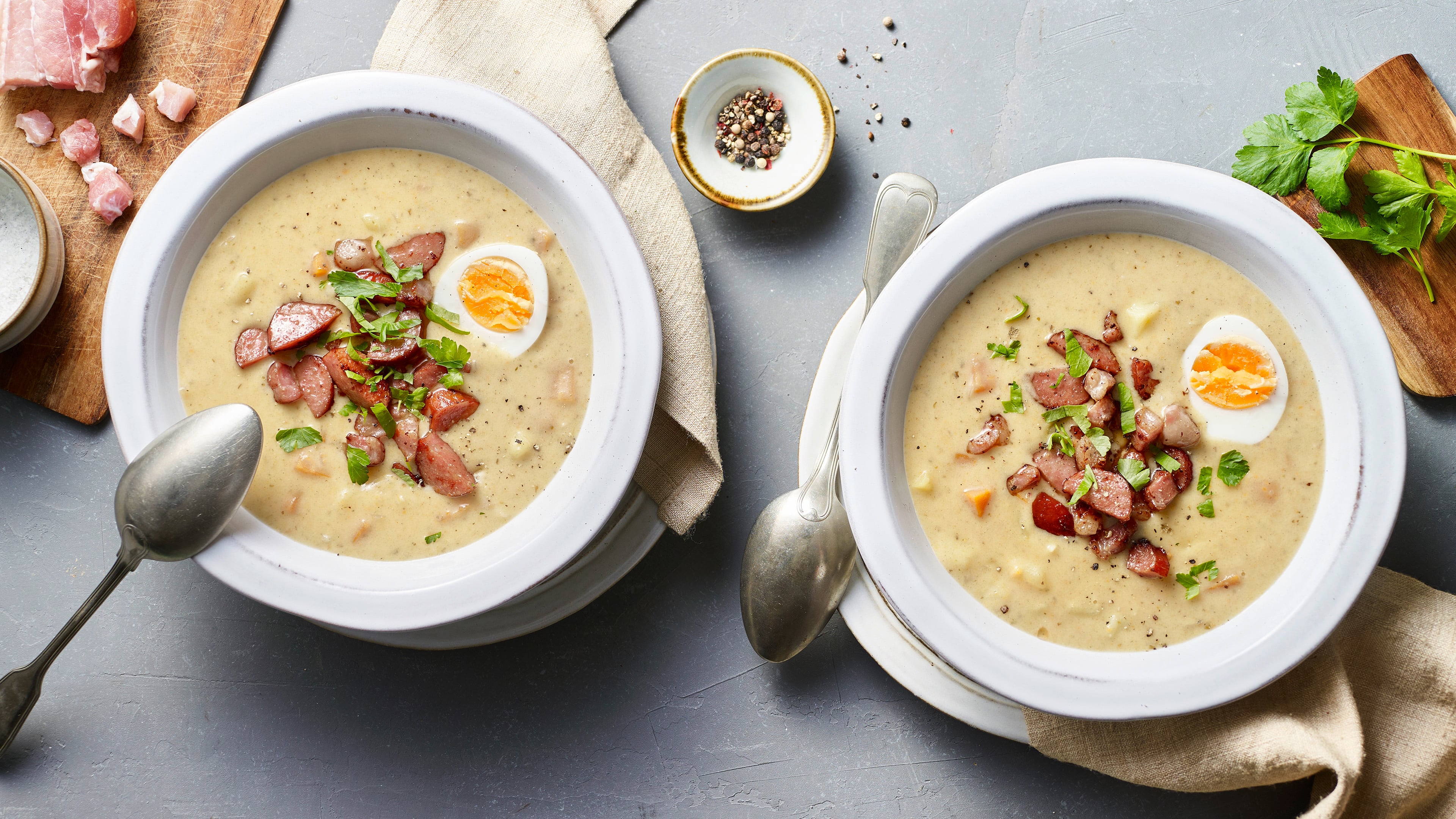 Polnisches Ostersuppen-Rezept für Zurek Cremige Suppe, getoppt mit Fleischstückchen, gekochtem Ei und gehackter Petersilie, in großen Suppentellern
