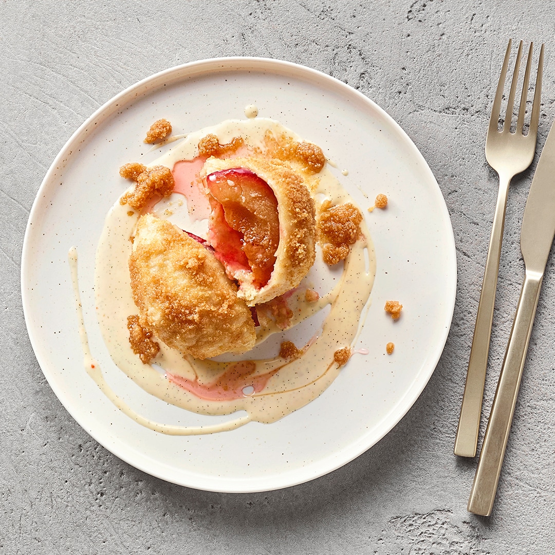 Geöffneter mit Früchten gefüllter Knödel auf Teller, daneben eine helle Soße