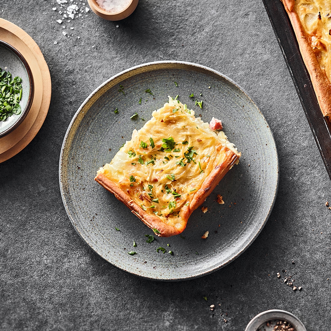Ein Teller mit einem Stück gelbgold gebackenen Zwiebelkuchen, getoppt mit frischer Petersilie