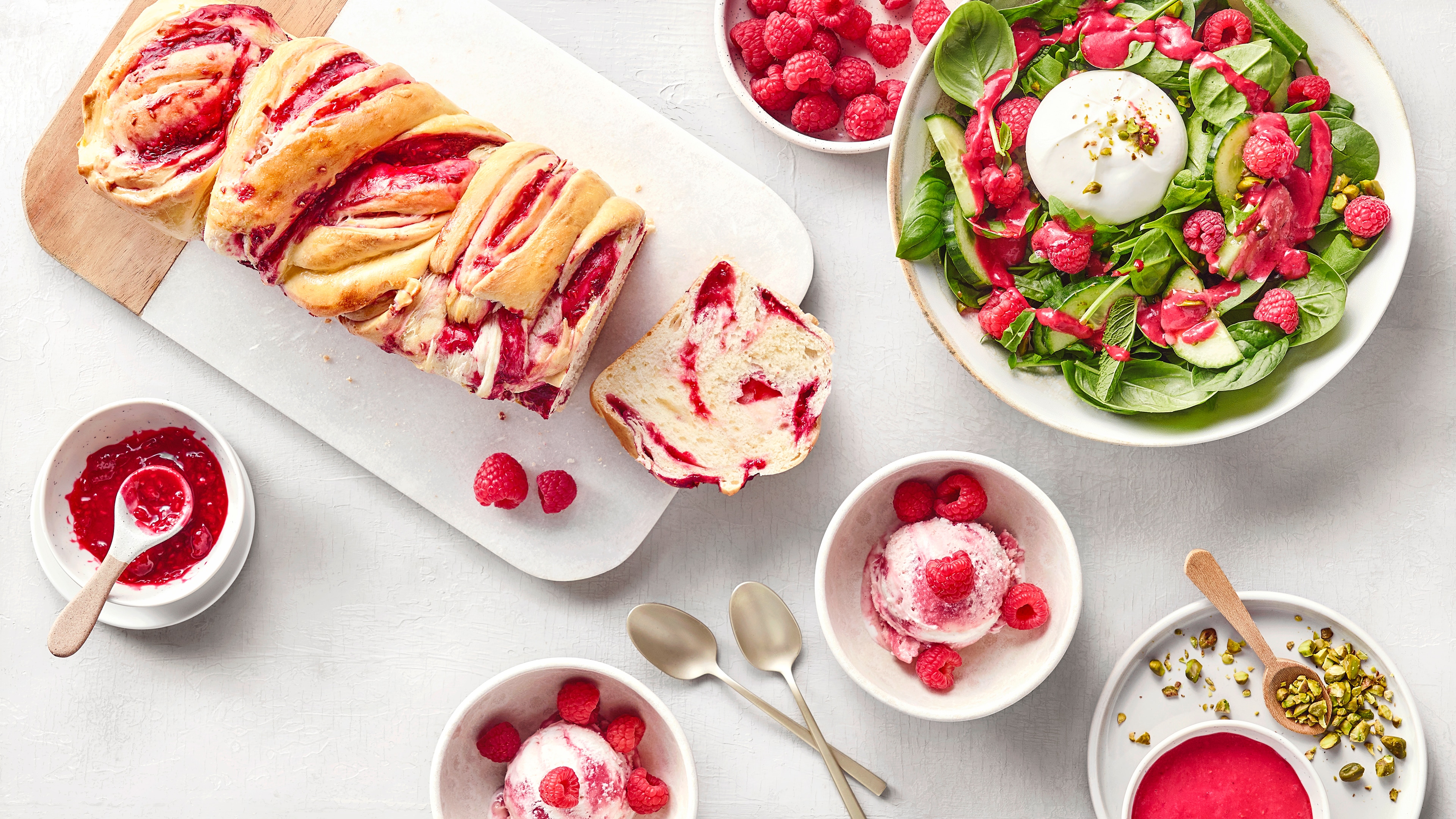 Viele Teller und Schalen mit Gebäck, Eis und Salat mit leuchtenden Himbeeren