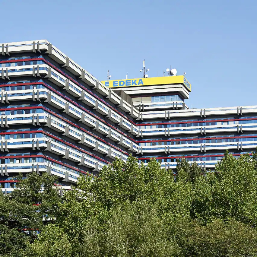 Gebäude der EDEKA-Zentrale in Hamburg vor blauem Himmel mit belaubten Bäumen im Vordergrund.