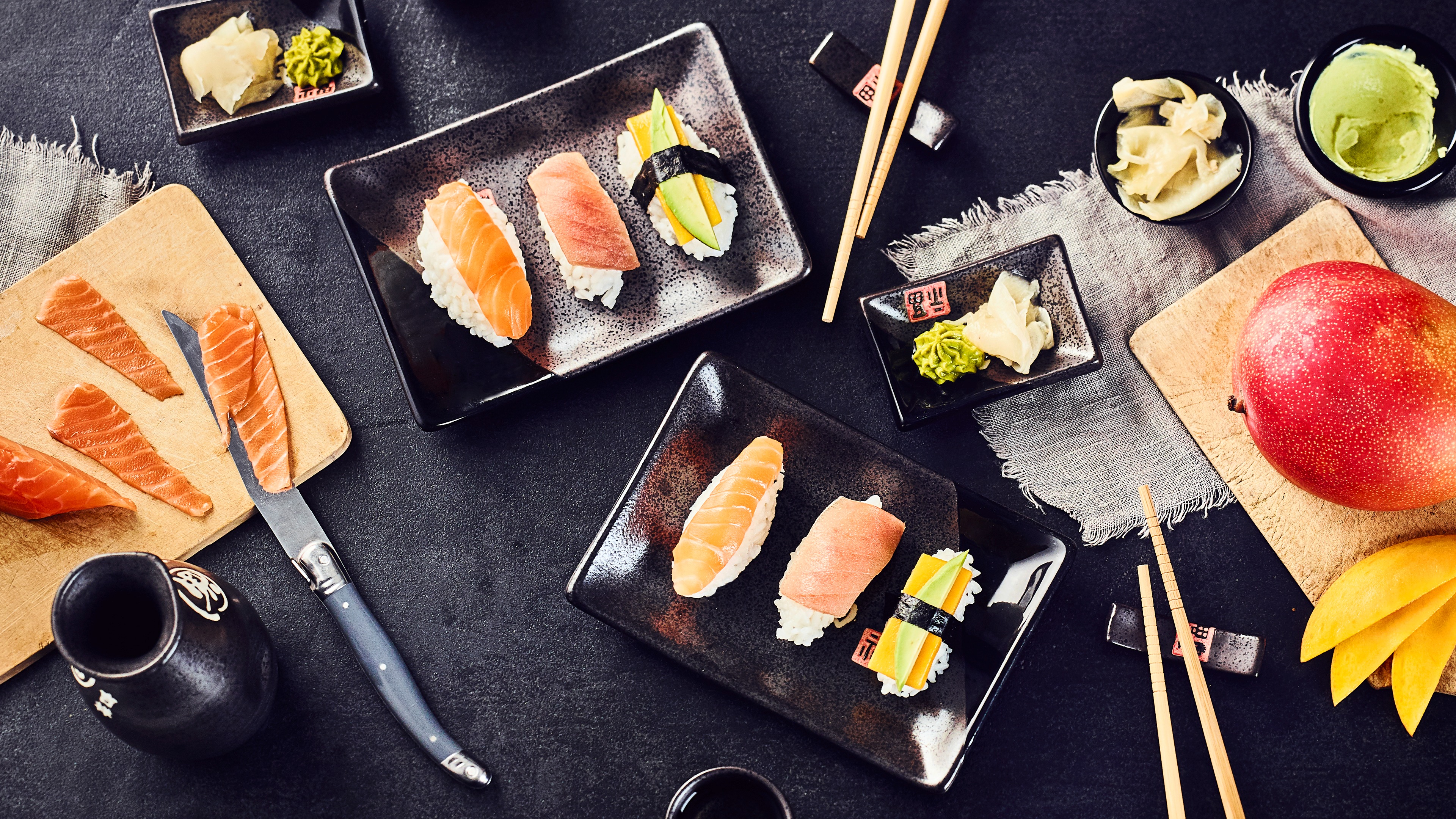 Auswahl an Nigiri-Sushi mit Lachs, Thunfisch und Avocado auf schwarzen Tellern.