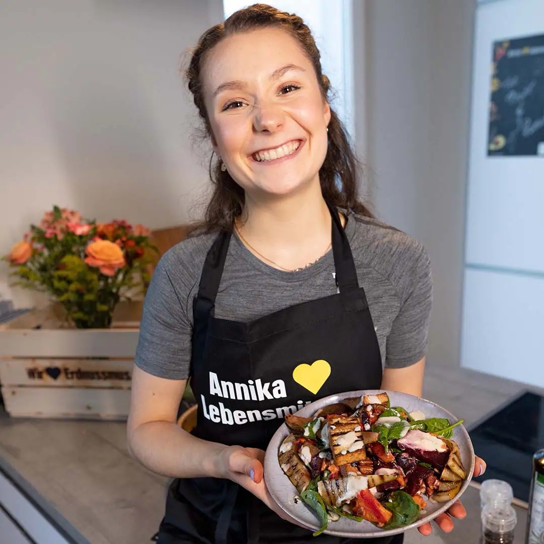 Junge Frau mit schwarzer EDEKA-Schürze präsentiert einen schön angerichteten Teller Essen.
