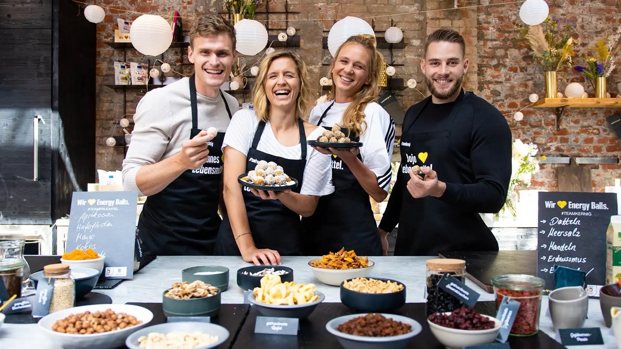 Gruppenbild mit zwei Männern und zwei Frauen, die an einer Küchenzeile ihre Snack-Balls präsentieren.