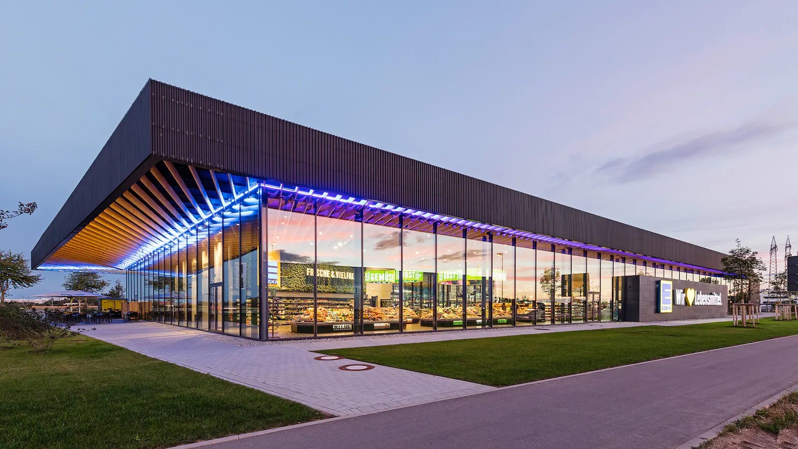 Mit lilanen LED-Leisten beleuchtete Fassade eines EDEKA-Marktes.