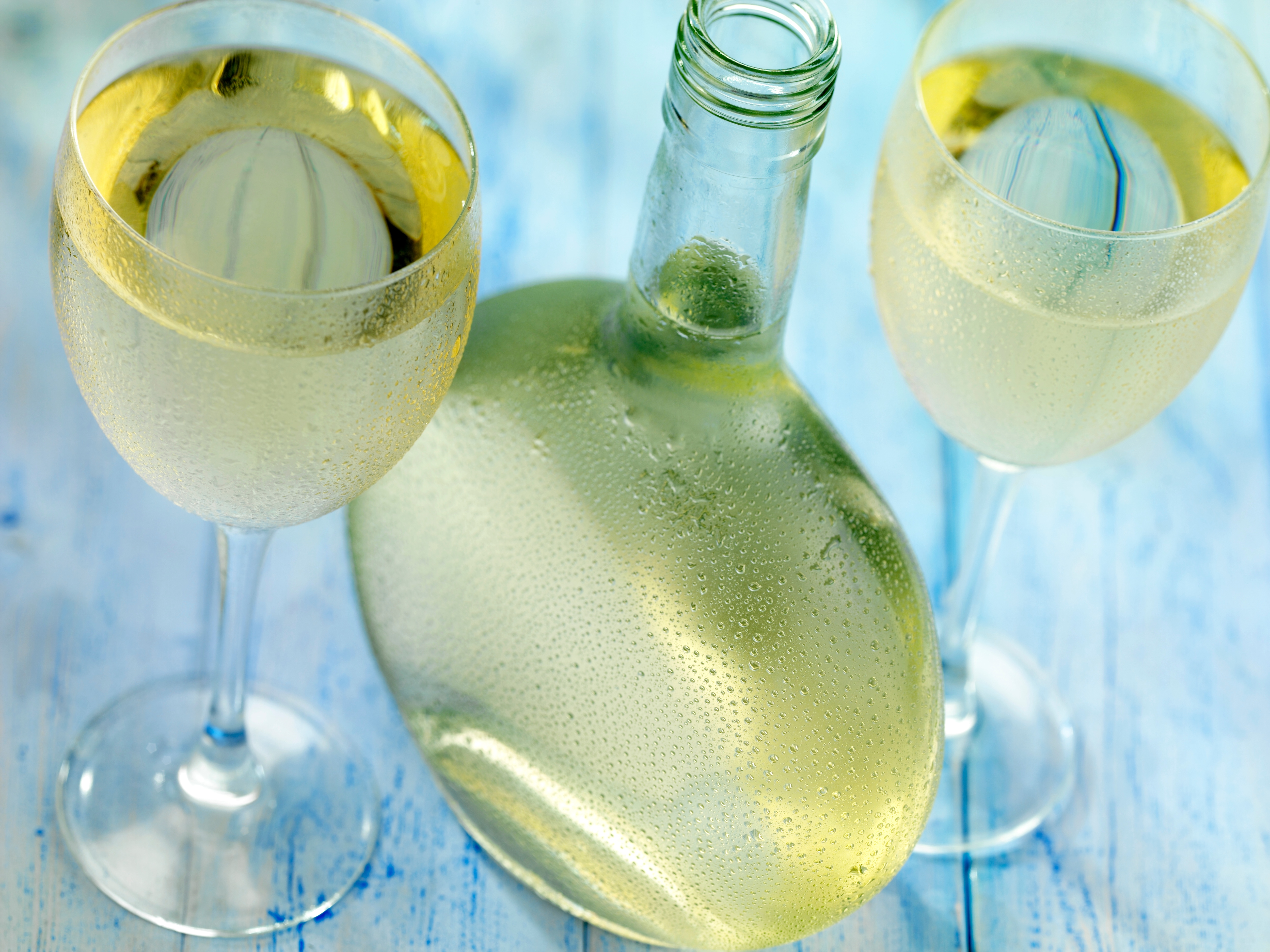 Zwei volle Gläser Weißwein mit einer bauchigen Flasche in der Mitte.
