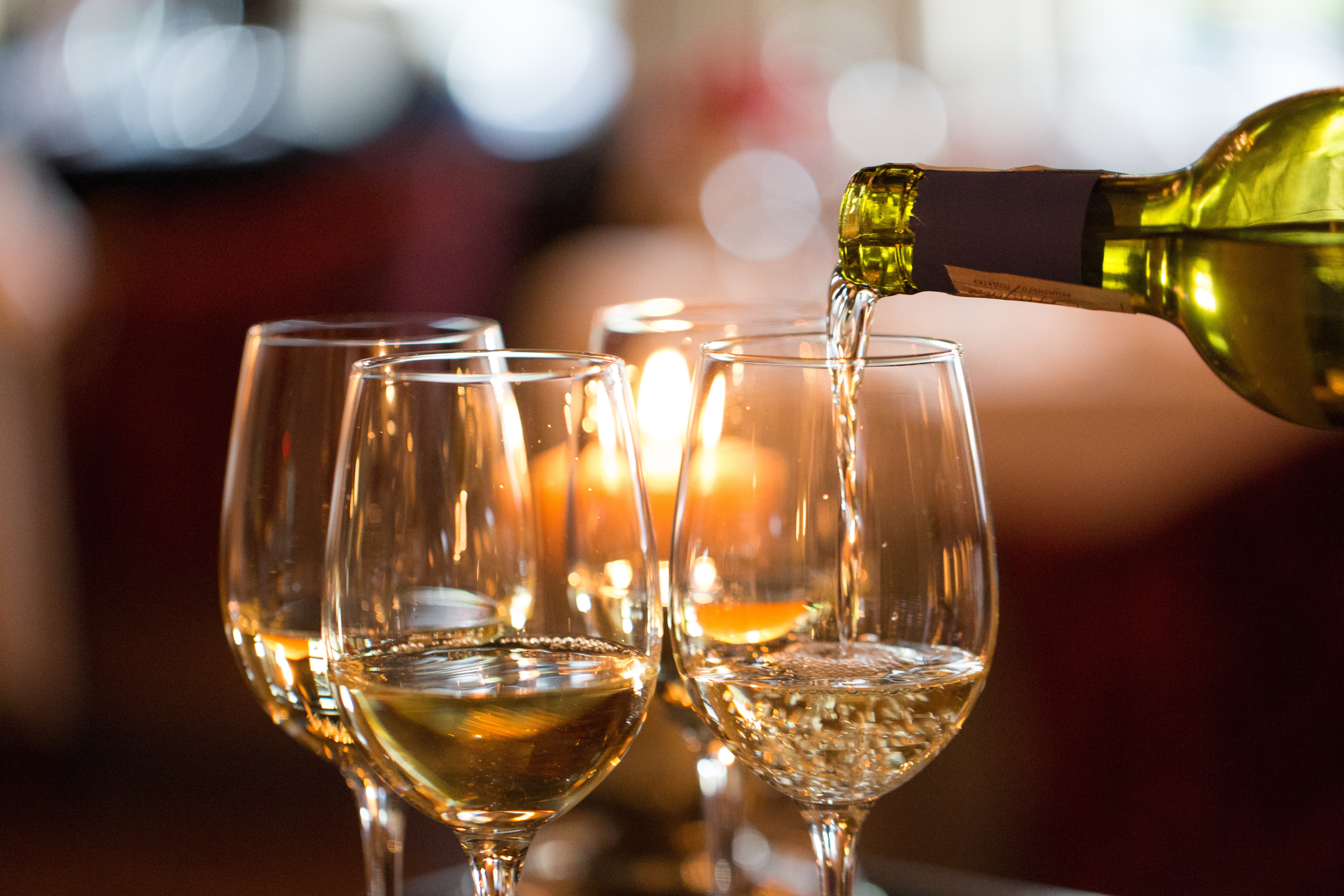 Mehrere glänzende Gläser werden mit Weißwein befüllt.