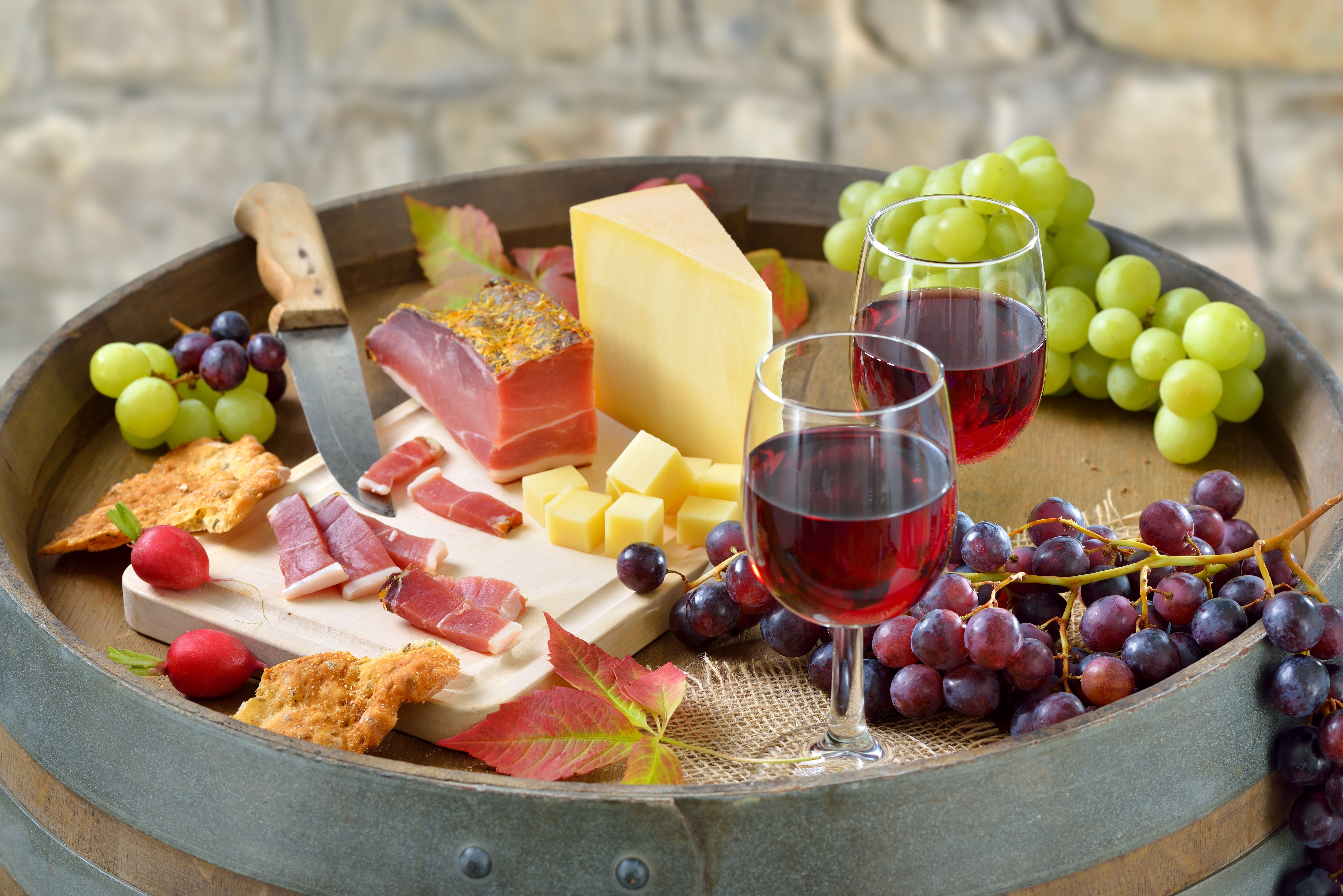 Zwei Gläser Rotwein auf Tablett mit Weintrauben, Schinken und Käse.