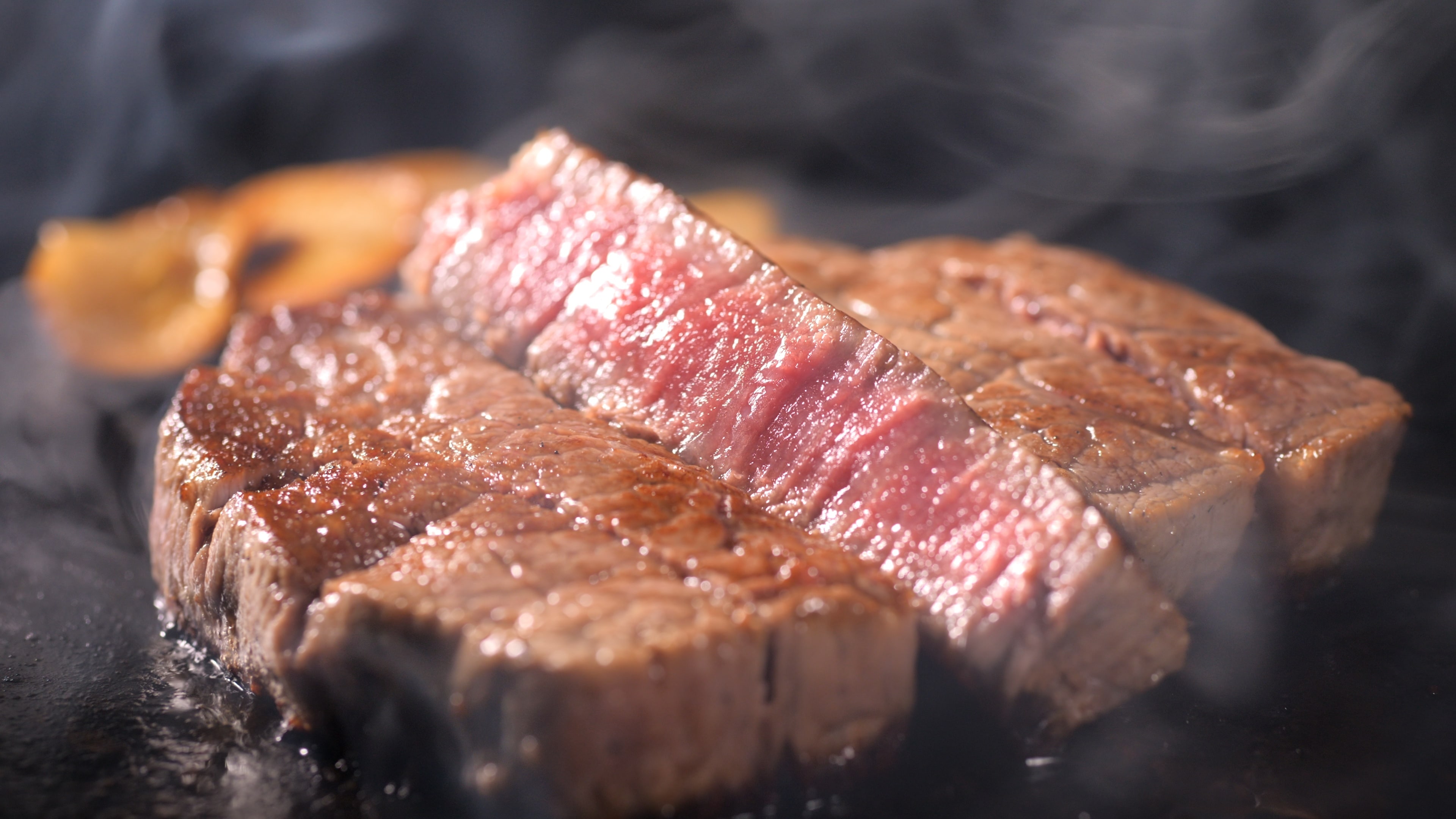 Gebratenes, saftiges Rindersteak mit rosa Kern auf heißer Grillplatte.