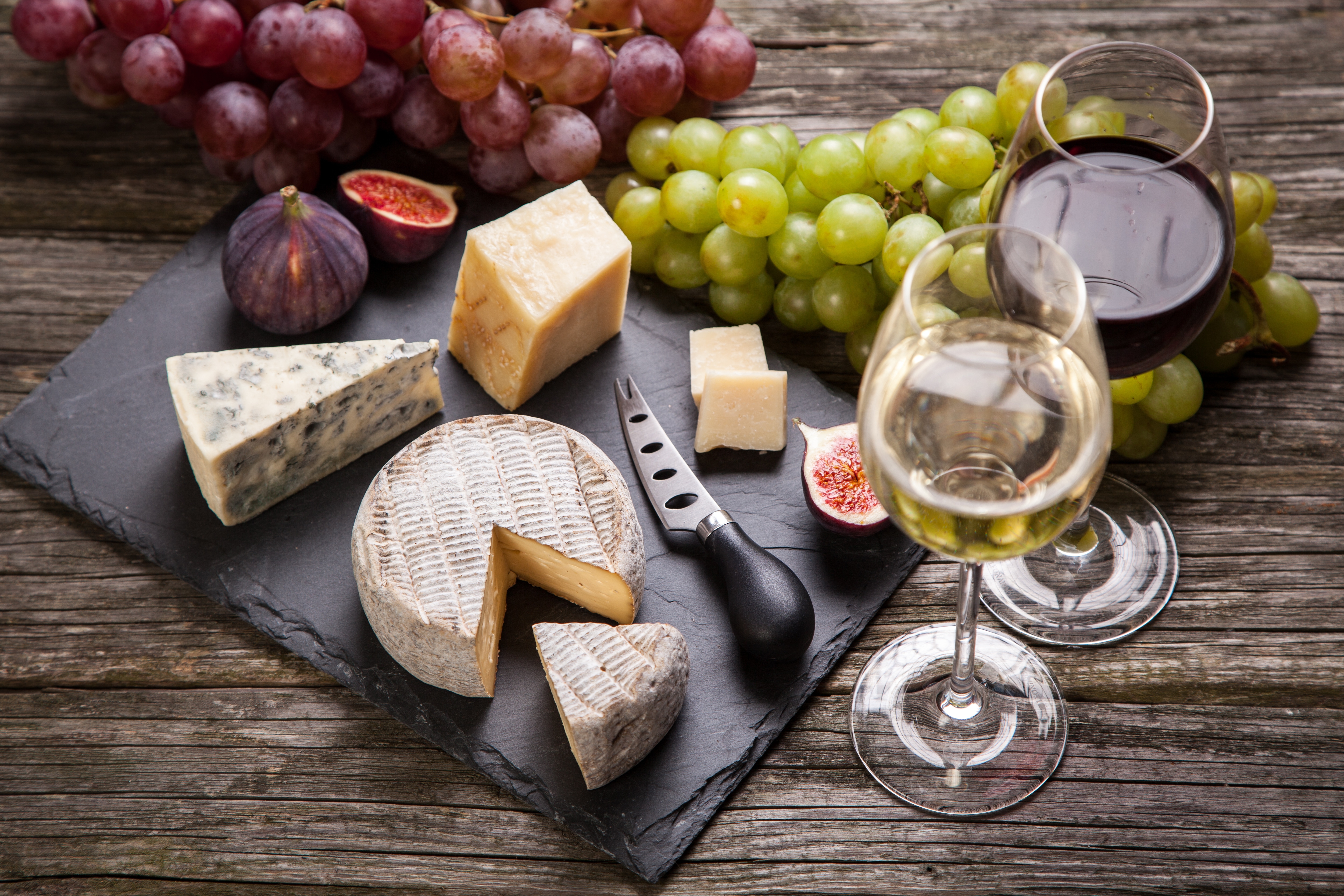 Ein Glas Weißwein und ein Glas Rotwein sowie eine Käseplatte und Weintrauben.